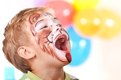 Happy little boy with lion face paint, enjoying birthday party. 