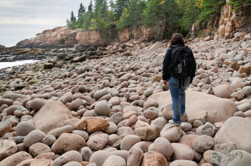Woman walking across a beach of large round stones.