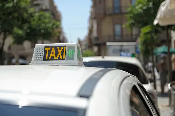Taxi in a Spanish City. There are some unrecognizable people standing on the sidewalk.