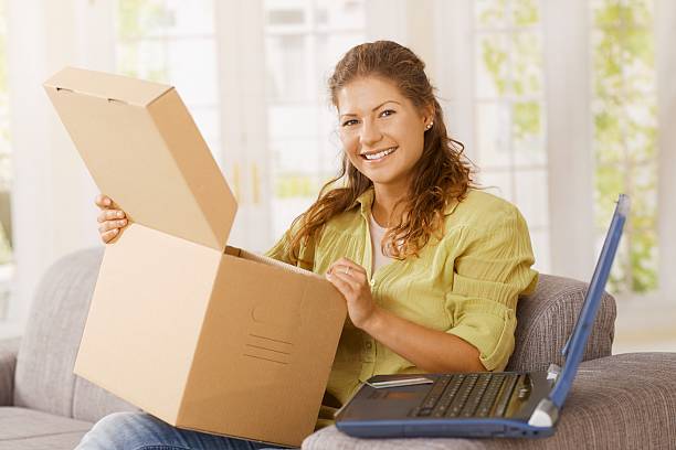 Happy young woman opening package at home stock photo
