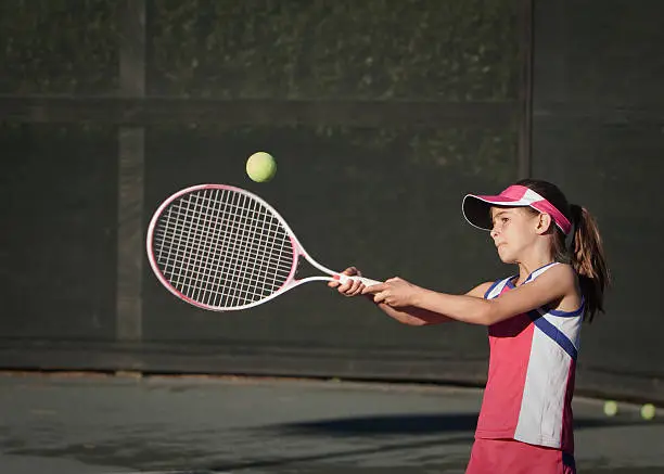 Little girl using all her power, keeping her eye on the ball, and hitting a tennis ball.