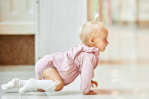 Small cute child crawling on the floor in a public place, shopping mall. Tiny blonde girl in pink dress smiling and having fun with mom while shopping. Funny weekend, happy childhood.