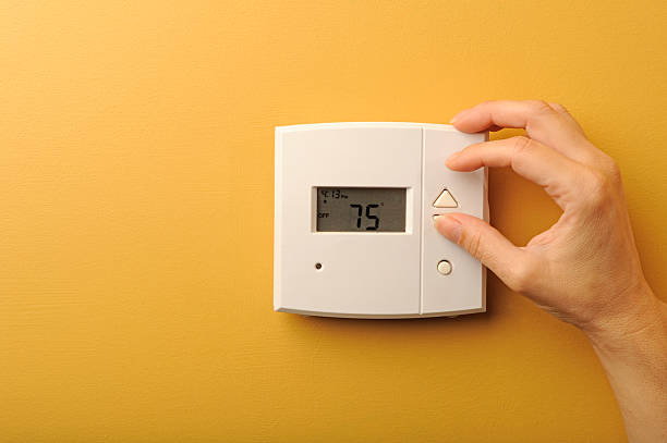 thermostat A woman turns down the thermostat. thermostat photos stock pictures, royalty-free photos & images