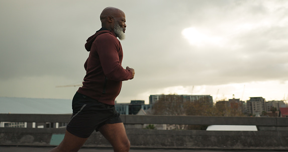 Man, city or senior runner with happy workout in training, fitness goals for health lifestyle. African athlete, retired and wellness or strong body for leisure in cape town, exercise or urban road
