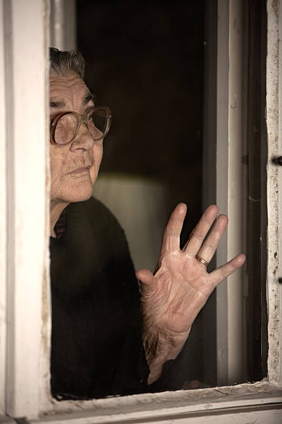 mulher idosa em pé e olhando pela janela fora - senior1 imagens e fotografias de stock