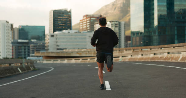男は、フィットネス、ワークアウト、マラソントレーニングのために、街、通り、橋で朝に背中を向けて走っています。ウェルネス、健康、またはトライアスロンのパフォーマンスのための� - marathon sport sports training city street ストックフォトと画像