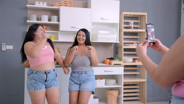 Cheerful mid adult overweight Asian female taking VDO recording of her two plus-size friends who singing and dancing at home.
Plus-size mid adult Asian women friends enjoy spending time together in a day. Fat friend.
