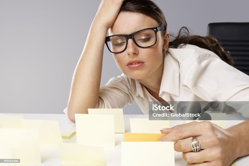 Cansado joven mujer de negocios hablando con notas pegarse en su escritorio - Foto de stock de 20 a 29 años libre de derechos
