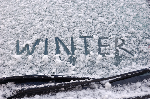 Winter motoring concept. Winter written in snow on car windscreen above windscreen wipers.