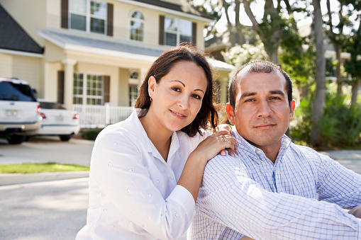 Happy mid-adult Hispanic couple sitting with house in background