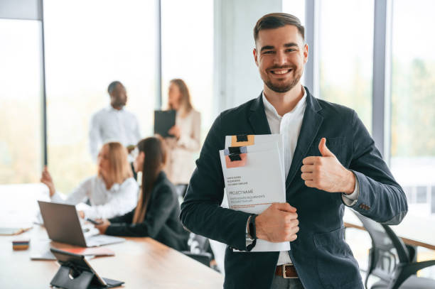 istock White man in suit is with papers in hands, standing. Group of office workers are together indoors 1832440270