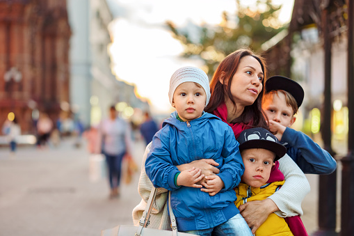 Busy mother with children group stands on city street. Woman and cute sons enjoys walk on town square. Large happy family with kids