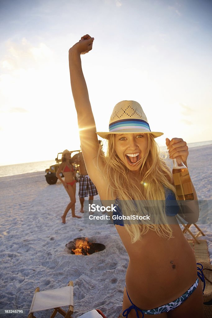 Junges Mädchen mit Bier und Freunden im Hintergrund am Strand - Lizenzfrei Bikini Stock-Foto