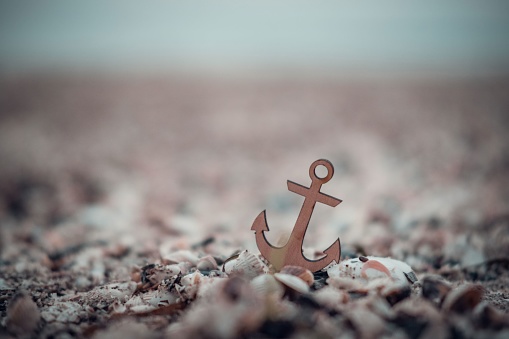 A miniature anchor amidst seashells on the Baltic Sea coast in Germany, a poetic symbol of stability and hope amidst the shifting sands of time