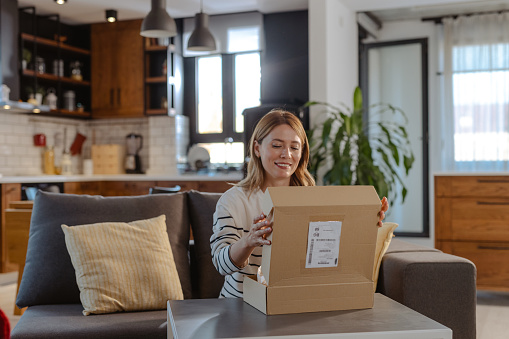 Beautiful woman with blond hair enjoying opening online delivery in the living room