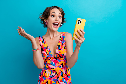 Photo of impressed ecstatic woman with bob hair dressed colorful clothes staring at sale in smartphone isolated on blue color background.