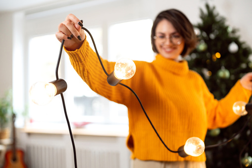 Portrait of an young Caucasian woman, decorating her home with big Christmas lights