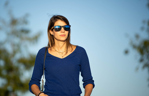 Relaxed woman wearing sunglasses and looking away while walking outdoors.
