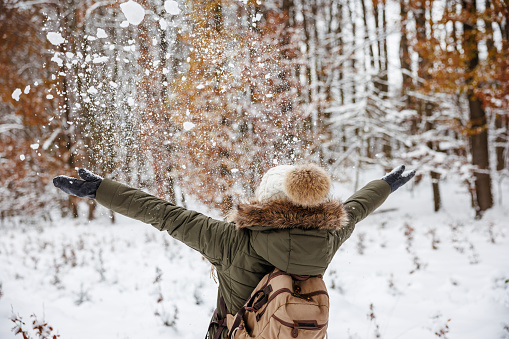 Cheerful woman playing with snow at winter forest. Happiness and mindfulness during enjoying walk outdoors