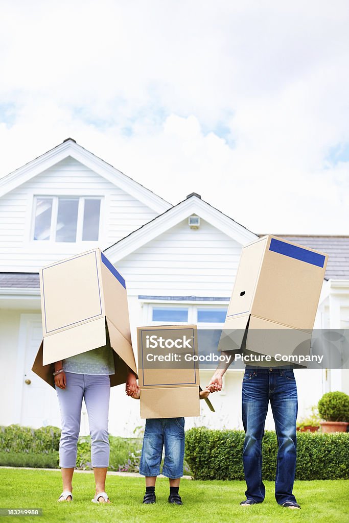 Family cover their faces with boxes in front of house Full length of family on grass while covering their faces with boxes in front of their house House Stock Photo