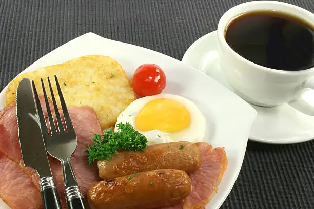 "Breakfast with bacon eggs, hash browns and coffee on black."