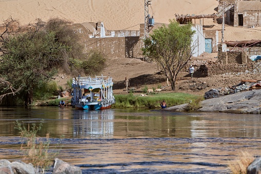 pueblo Nubio, Egypt – September 26, 2023: A unique boat sailing downriver near a quaint mountain village in Egypt.