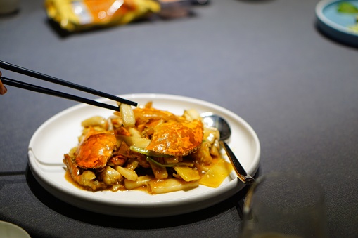 A close-up of a person enjoying a plate of seafood, with crab and other seafood using chopsticks
