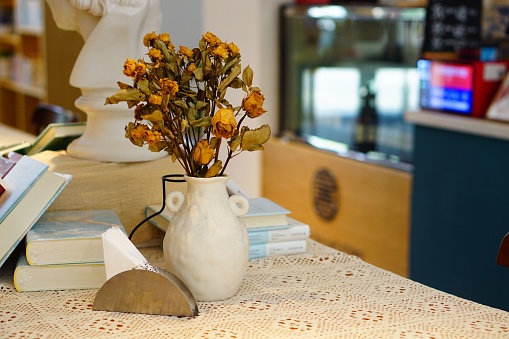 An arrangement of dried flowers in a glass vase placed on a wooden table next to several books