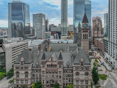 Drone-shot of Toronto Old City Hall, showcasing its clock tower and masonry against a backdrop of modern skyscrapers.