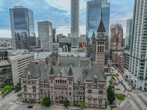 Drone-shot of Toronto Old City Hall, showcasing its clock tower and masonry against a backdrop of modern skyscrapers.
