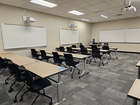 An empty classroom interior, with rows of desks and a projector suspended from the ceiling