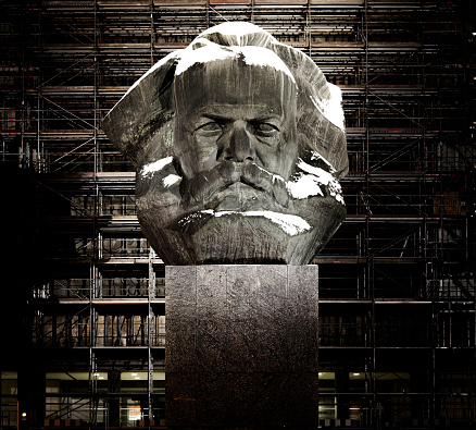 Chemnitz, Saxony, Germany on December 3, 2023: The Karl Marx Monument is a 7.10m (23.29ft)-tall stylized head of Karl Marx in Chemnitz, Germany. The heavy-duty sculpture, together with the base platform, stand over 13 meters (42 feet) tall and weighs approximately 40 tonnes. On a wall just behind the monument (behind the scaffolding, currrently in renovation)  the phrase \