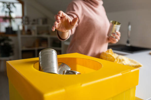A mature Caucasian woman putting tin cans in a cardboard box to reuse later in the kitchen of her apartment