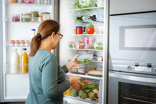 Woman takes container with fresh vegetables from fridge