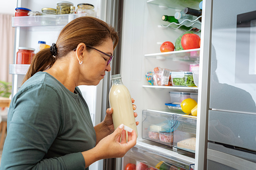 Disgusted woman smelling expired milk by the fridge