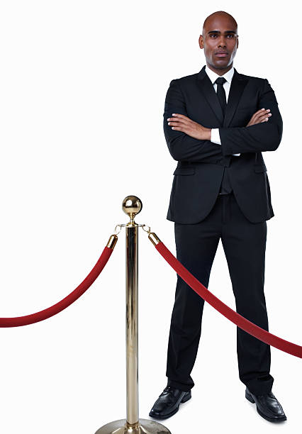 Bouncer in suit standing behind crowd control post against white Full length of a bouncer in suit standing behind crowd control post against white - copyspace bouncer security staff stock pictures, royalty-free photos & images