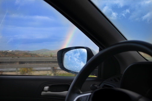 Travel concept with rainbow background. Driving a car a beautiful blue sky and seeing rainbow