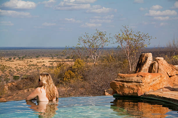 Blond girl looks out over the African savannah from a raised safari lodge infinity pool