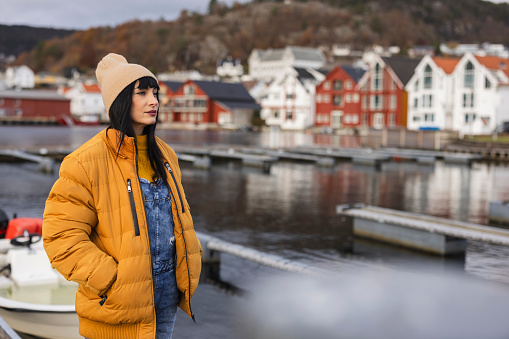young adult woman in yellow coat contemplating the skyline in the harbor of a city in Norway