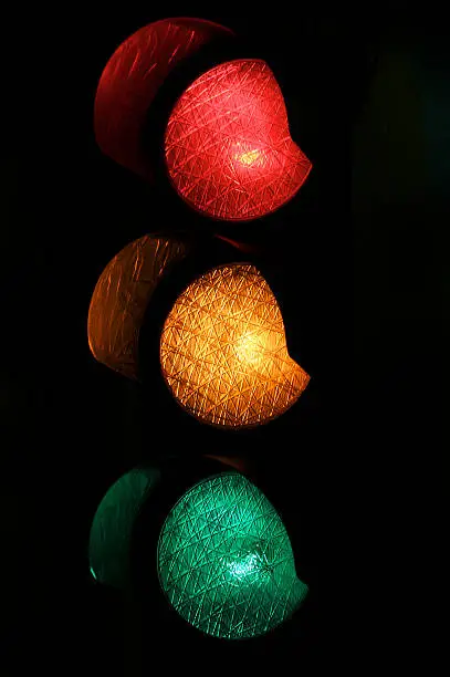 Traffic light stoplight with red, yellow, and green lights all glowing against a dark background