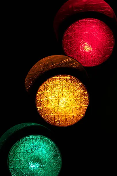 "Stoplight with all lights glowing red, yellow, and green against dark background"