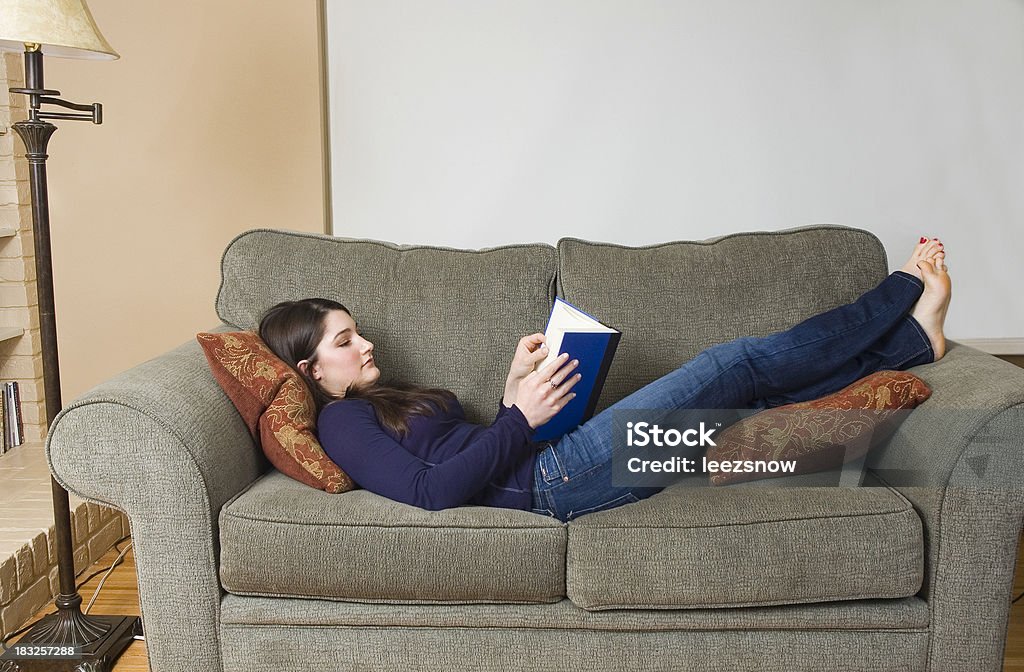 Teenage Girl Reading en el sofá en la sala de estar - Foto de stock de Acostado libre de derechos