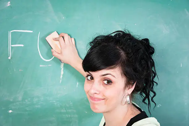 A teacher erases profanity from a blackboard in a school classroom.
