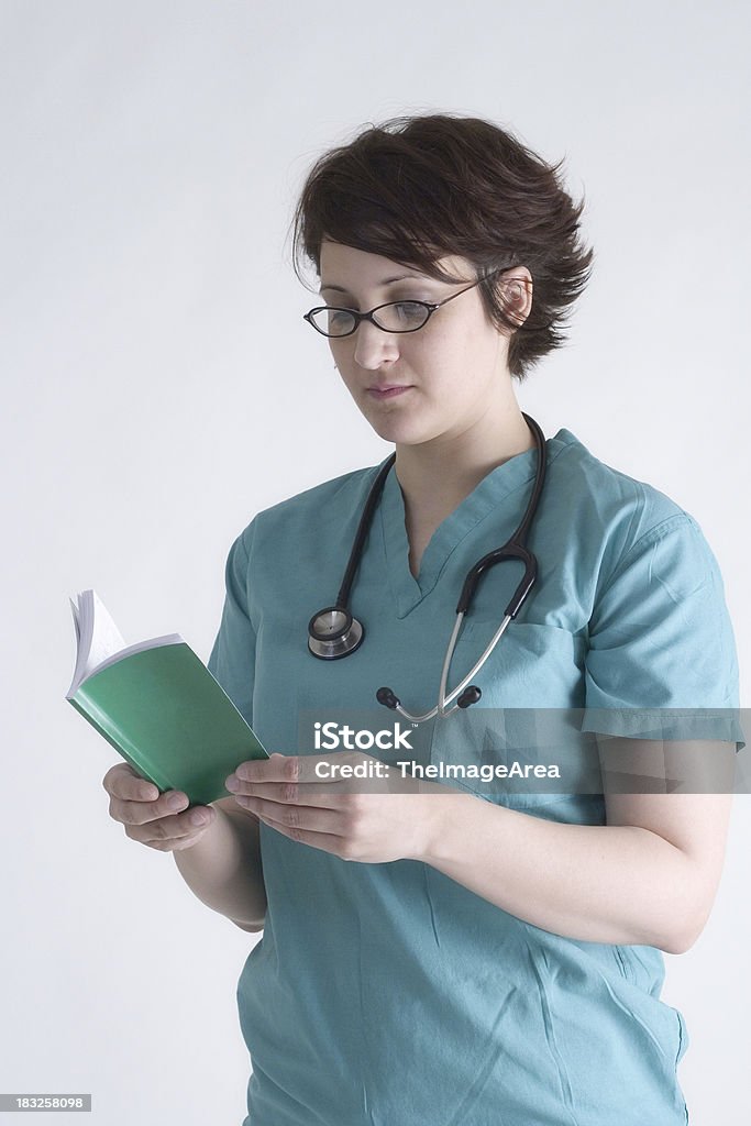Nurse reading medical reference guide Nurse wearing glasses and scrubs reading a medical reference guide Accidents and Disasters Stock Photo