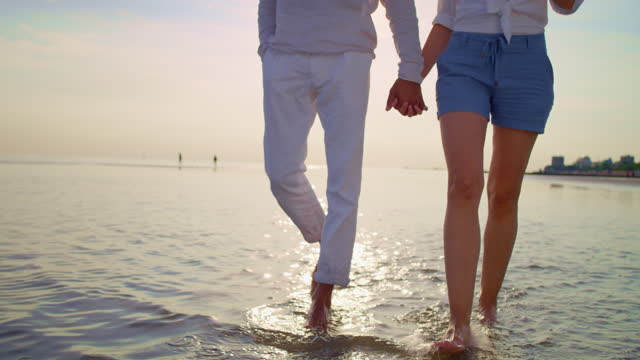 SLO MO TS Man and woman holding hands and walking barefoot on the sandy beach