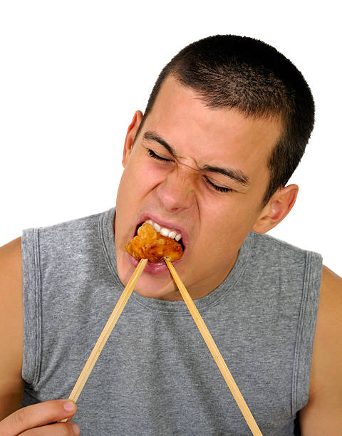 Teen Learning to Use Chopsticks (Isolated on White) "Young man, 19 year-old teen, struggles with chopsticks in this scene, but it should be noted he is an expert user." mike cherim stock pictures, royalty-free photos & images