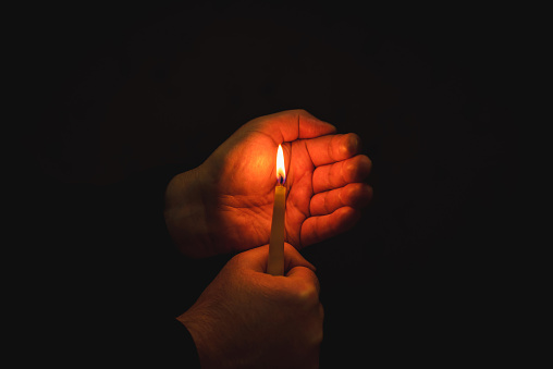 Burning candle in male hand, religion concept.Black background.