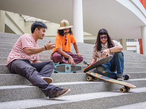 Small Group of young Asian skateboarder man holding and discussing while sitting on the stairs at outdoors, People and Active lifestyle