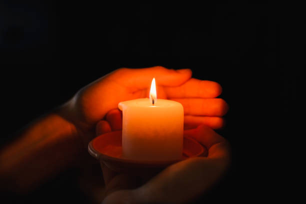 istock Religious concept.Boy holds in a hand a burning candle against black background. 1832602328