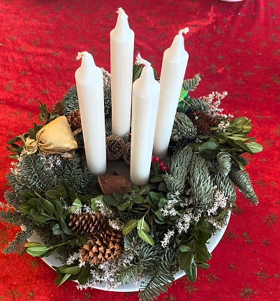 Christmas advent wreath in dark room in front of white cabinets with all four candles lit, red berries and evergreen boughs on wreath